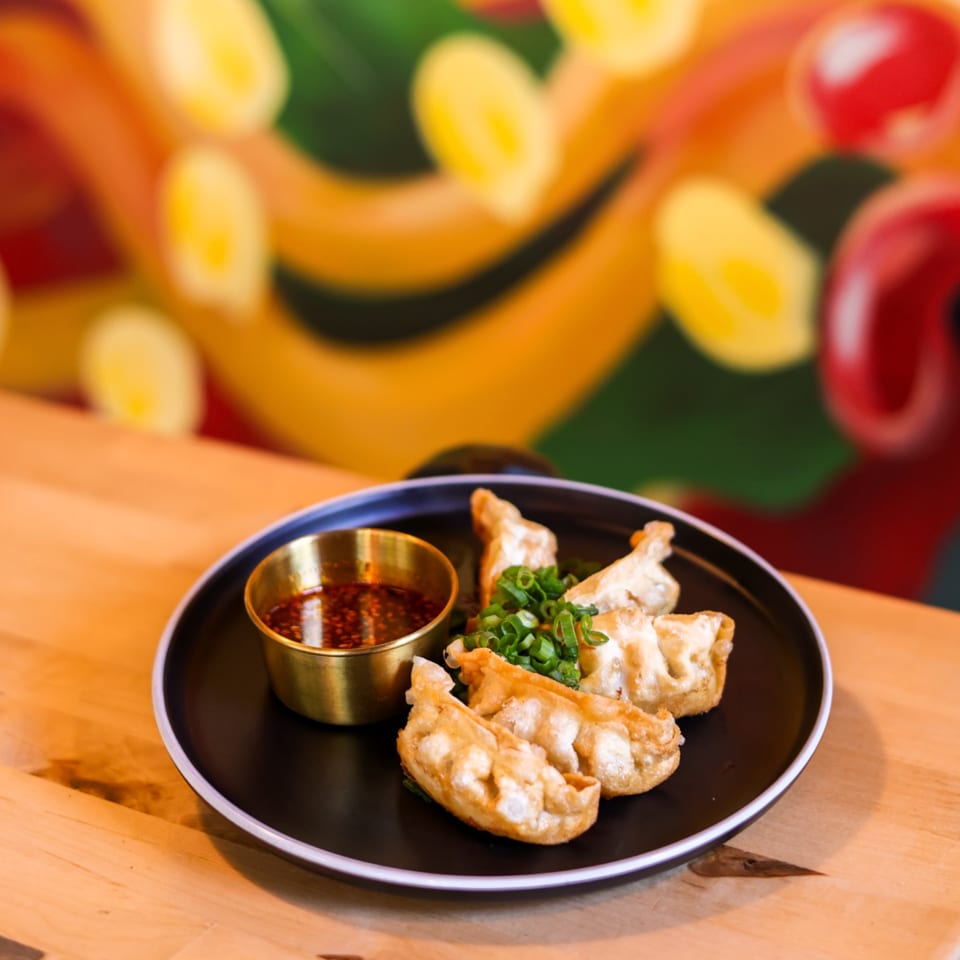 Crispy fried dumplings with green onions and a side of chili oil on a black plate.