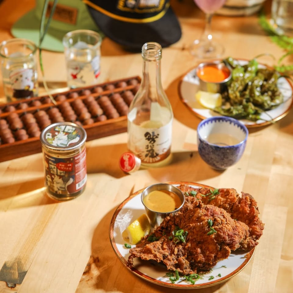 Fried chicken with sauce and lemon, shishito peppers, sake, and an abacus on a wooden table.