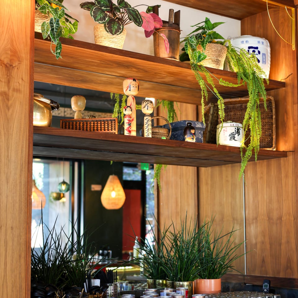 Wooden shelves adorned with potted plants, Japanese kokeshi dolls, and traditional decor, reflecting warm lighting.