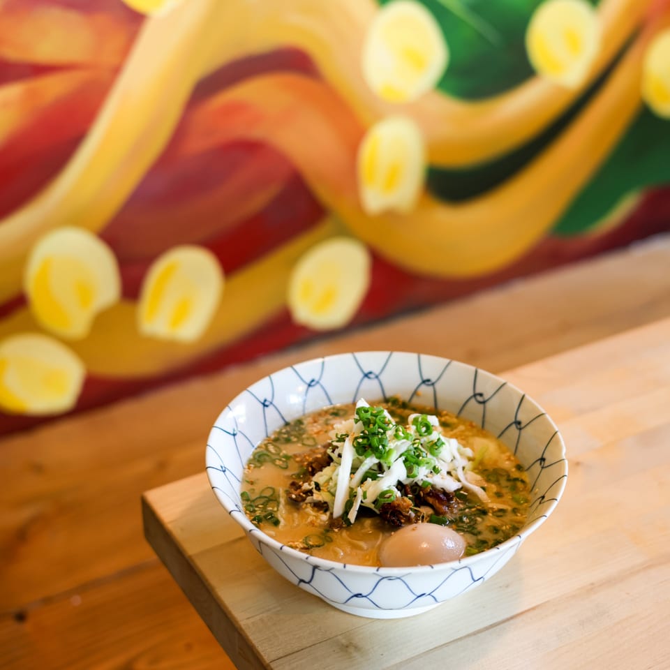 A bowl of ramen with green onions, cabbage, and an egg on a wooden table.